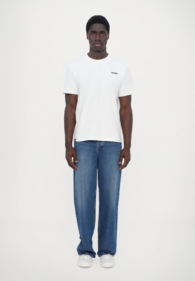 White cotton t-shirt with a black logo, paired with loose blue denim jeans and white sneakers. Simple design, no distinct patterns or accents.