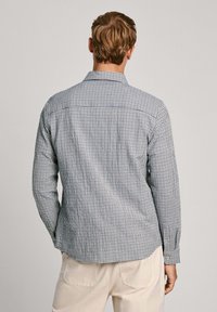 Camisa a cuadros en azul y blanco. Material de algodón, de manga larga, con cuello estándar y dobladillo curvado. Presenta un pliegue central en la parte posterior.