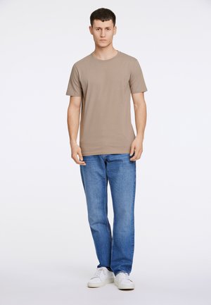 T-shirt beige in cotone con collo rotondo, maniche corte e design aderente, abbinato a jeans blu a gamba dritta e sneakers bianche.