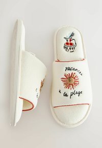 Zapatillas de tela blancas con un sol bordado, jarra y texto en francés "Vacances à la plage" en la parte superior, mostradas lado a lado.