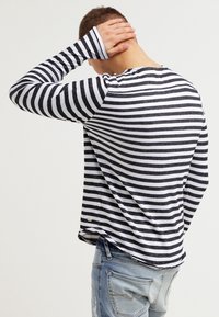 Zwart-wit gestreepte lange mouw shirt, met een ronde halslijn, zachte textuur en zijsplitten, gedragen met versleten lichtblauwe jeans.