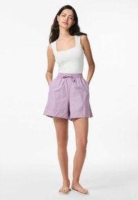 Top bianco senza maniche abbinato a pantaloni corto a righe viola e bianche con vita elastica e tasche laterali. Sandali piatti indossati.