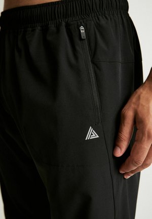 Pantaloni atletici negri cu un talie elastică, buzunar cu fermoar pe lateral și un logo mic, triunghiular, argintiu, în față.