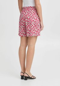 Pantaloni corti floreali con una base bianca, caratterizzati da pattern rossi e verdi. Vita elastica, lunghezza sopra il ginocchio, abbinati a sandali neri con tacco a blocco.