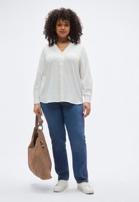 Άσπρο πουκάμισο με μακριά μανίκια και κουμπιά, με υφή, συνδυασμένο με μπλε τζιν και καφέ σουέτ τσάντα tote. Άσπρα αθλητικά παπούτσια ολοκληρώνουν το σύνολο.