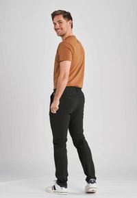 Ruskea puuvillainen crew-neck t-paita yhdistettynä mustiin slim-fit-housuihin ja valkoisiin lenkkarit. Malli on kääntynyt hieman, jolloin asun selkäosa näkyy.