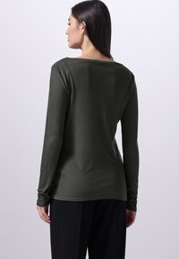 Langärmliges, geripptes Shirt in Dunkelgrün mit weitem Halsauschnitt, glatter Textur und figurbetontem Schnitt, kombiniert mit lockeren schwarzen Hosen.