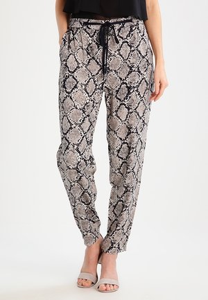 Woman wearing snake print pants with black drawstring and beige open-toe heels, standing against a plain light background.