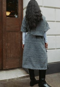 Hall triibuline komplekt, millel on lahtine ülaosa ja sobiv seelik. Omab lühikesi varrukaid ja keskmise pikkusega ääreosa. Mustad põlveni ulatuvad saapad.