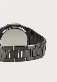 Montre bracelet noire avec un bracelet en métal à maillons rectangulaires. Boîtier rond avec une couronne en or et un dos métallique lisse.