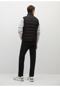 Černá puffer vesta s vysokým límcem, šedé texturované rukávy a elegantní design, doplněná o tmavé kalhoty a bílé tenisky.