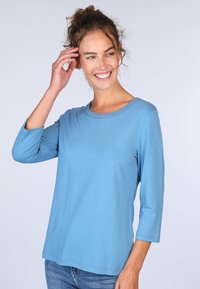 Helles blauer Langarmtop mit rundem Ausschnitt, weicher Textur und lockerer Passform. Verfügt über dekorative Nähte entlang des Ausschnitts.