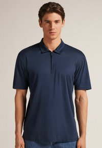 Granatowa koszulka polo z krótkim zamkiem, uszyta z gładkiego materiału. Posiada klasyczny kołnierzyk oraz krótkie rękawy w luźnym kroju.