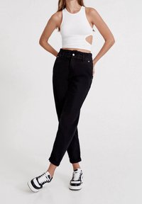 Svarta högmidjade jeans med avslappnad passform, med en cinchad midja och uppvikta fållar. Kombineras med en vit crop top med utskärning och svarta sneakers.