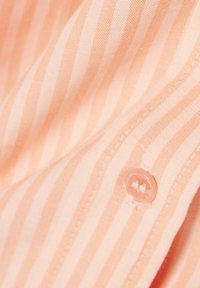 Primer plano de una tela con rayas verticales en tonos naranja pálido y blanco, con un botón transparente cosido sobre ella.