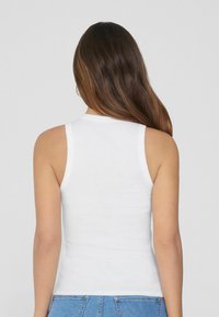 Top sin mangas blanco de canalé con un diseño ajustado, que presenta un cuello redondo y se combina con unos jeans de mezclilla de tiro alto en azul.