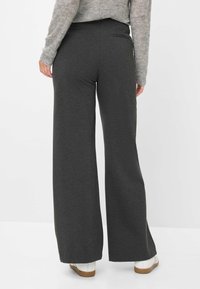 Weite, dunkelgraue Hosen aus weichem Stoff mit glatter Oberfläche und seitlichen Taschen, kombiniert mit weißen Schuhen und einem hellen Pullover.