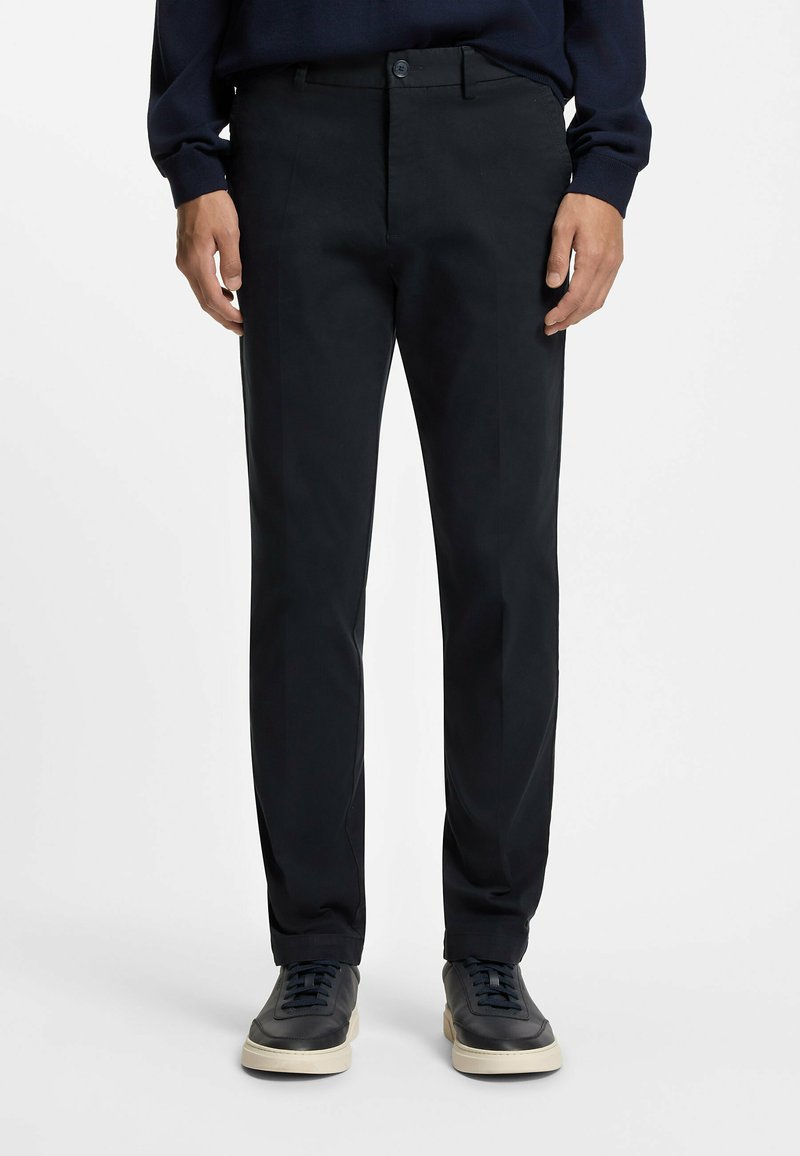 Czarne spodnie o dopasowanym kroju, z płaskim przodem i dwoma bocznymi kieszeniami. Noszone z ciemnymi sneakersami, mają gładkie wykończenie i subtelną fakturę.