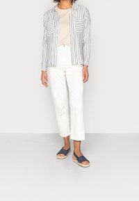 Pruhovaná košile na knoflíky v bílé a šedé barvě, béžový top, bílé cropped kalhoty a námořnické slip-on sandály s tkanou podrážkou.