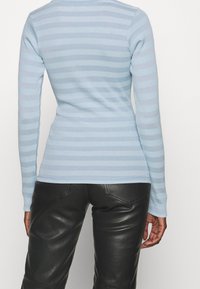 Himmelblaues Langarmoberteil mit horizontalen Streifen, gerippten Texturen und taillierter Silhouette, kombiniert mit schwarzen Lederhosen.