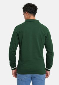 Polo de manga larga en algodón verde oscuro. Cuenta con un collar clásico, rayas blancas en los puños y un dobladillo recto con ligera textura.