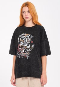 Camiseta negra de gran tamaño en tela lavada con un diseño colorido impreso en pantalla que presenta patrones intrincados de animales y naturaleza.