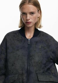 Navy bomber jacket with floral embroidery, ribbed neckline, front zipper, and two side pockets; lightweight fabric with a textured appearance.