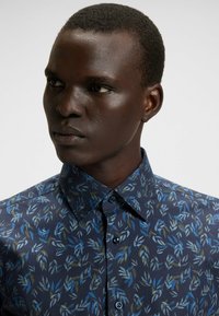 Marineblauw overhemd met een bladerenpatroon in blauwe en groene tinten, voorzien van een button-down kraag en een gladde textuur.