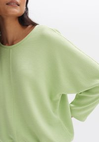Hellgrünes, geripptes Oberteil mit lockerer Passform, rundem Halsausschnitt und 3/4-Ärmeln, das über eine subtile Textur und glattes Material verfügt.