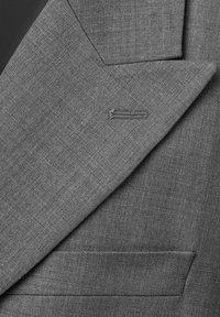 Nærbillede af gråt stof på en jakkeslætets revers med en knaphul og lomme, der viser en fin tekstureret vævning og skræddersyede syninger.