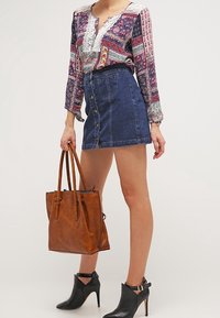 Blusa a maniche lunghe con motivo e rifiniture in pizzo, abbinata a una gonna di jeans con bottoni frontali, borsa a tracolla in pelle marrone e stivaletti neri con tacco.