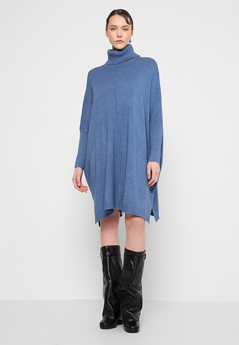 Blaues Rollkragenkleid mit lockerer Passform, gerippten Ärmelsäumen, seitlichen Schlitzen und weicher Textur, kombiniert mit schwarzen kniehohen Stiefeln.