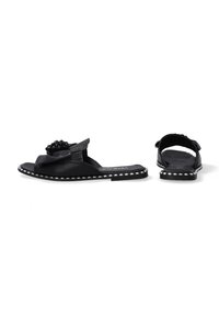 Zwarte sandalen met een textuurriem en decoratieve zwarte kraalaccenten. Kenmerkt zich door een platte zool met een zilvergestikte rand en een open achterkant.