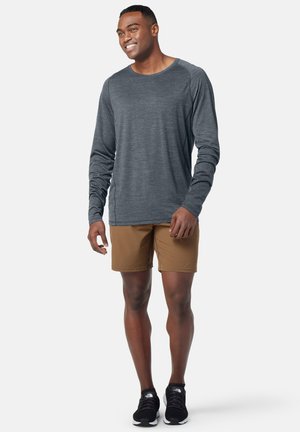 Maglietta a maniche lunghe grigia scura, leggera, abbinata a pantaloni corti beige e sneakers nere. Design semplice, vestibilità rilassata, adatta per un abbigliamento casual.