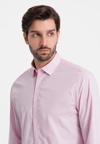 Camisa de dress rosa claro con cuello clásico, frente abotonado y textura de tela suave. Presenta mangas largas y sutiles detalles de costura.