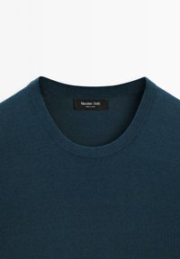Pull col rond bleu sarcelle foncé avec une texture fine tricotée, montrant l'étiquette intérieure indiquant "Massimo Dutti Made in China."