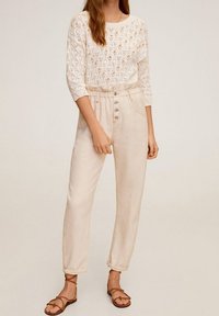 Jasnobeżowe lniane spodnie o luźnym kroju i elastycznym pasie, z zapięciem na guzik oraz dwiema bocznymi kieszeniami. Noszone z białym wełnianym topem.