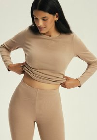 Beżowa, prążkowana koszulka z długim rękawem w połączeniu z legginsami o wysokim stanie, wykonanymi z miękkiego, elastycznego materiału, tworząc dopasowaną sylwetkę.