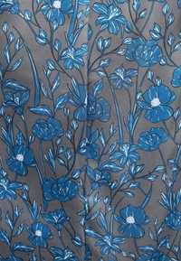 Diseño floral azul sobre una tela gris, que presenta varias flores y hojas con contornos detallados. La textura parece suave y tejida.