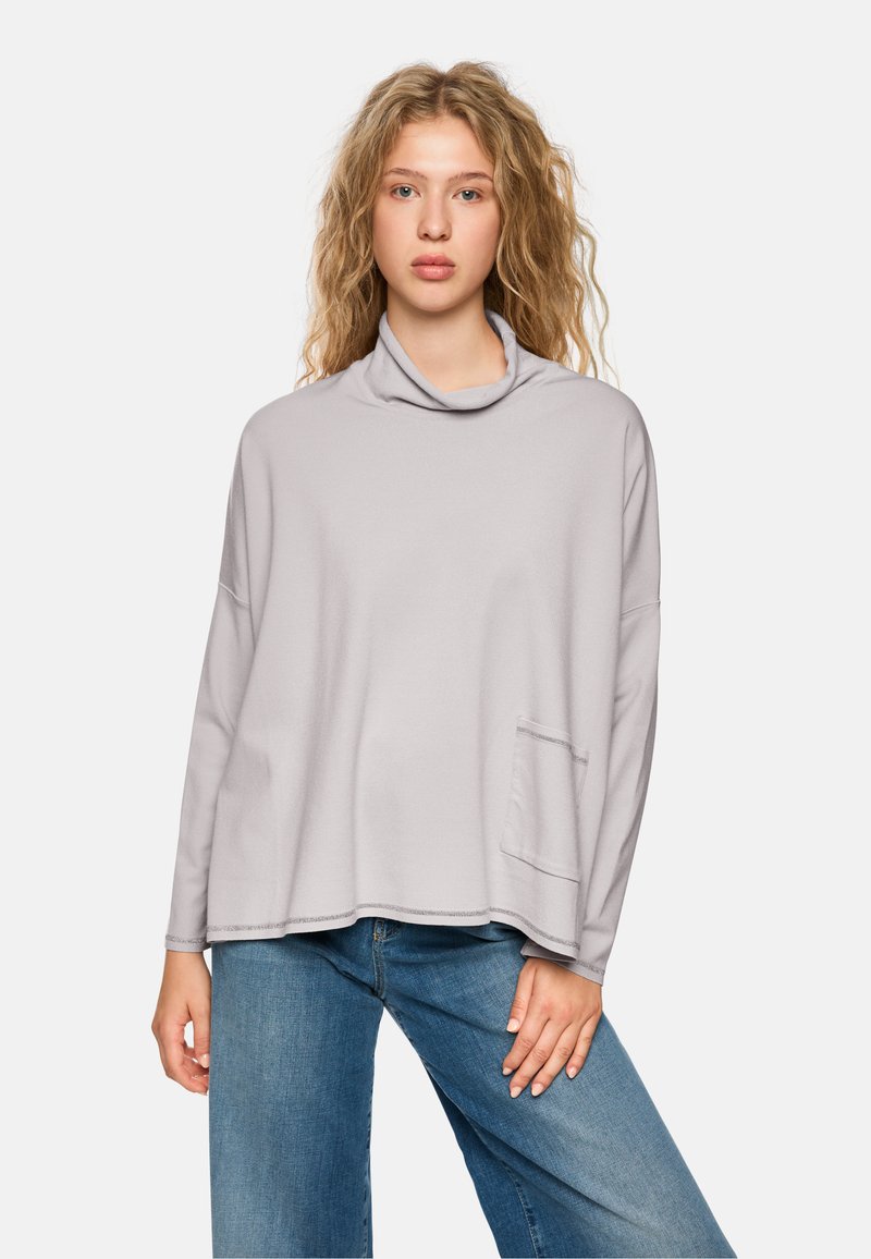 Hellgrauer Pullover mit Kapuze und langen Ärmeln, lockerer Schnitt, ausgestattet mit einer Fronttasche und sichtbaren Nähten. Kombiniert mit blauen Jeans.