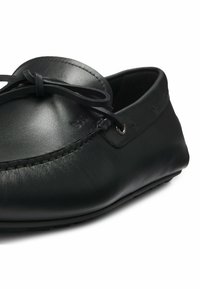 Czarne skórzane mokasyny o gładkiej teksturze, z okrągłym noskiem, przeszyciami oraz akcentem w postaci kokardy na wierzchu.