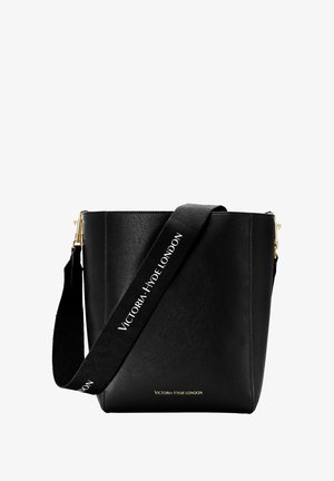 Musta nahkainen bucket-laukku, jossa leveä merkitty olkahihna ja kultaiset metalliosat. Edessä ja hihnassa lukee "Victoria Hyde London".
