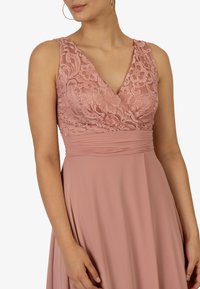 Abito rosa con un corpetto in pizzo con scollatura a V, vita plissettata e gonna morbida. Il materiale ha una consistenza soffice con un design fluido.
