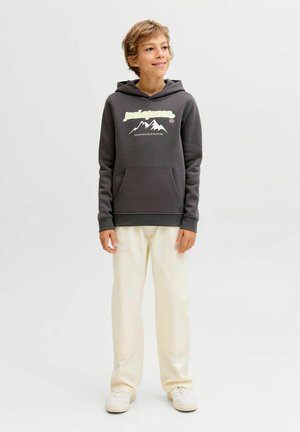 Felpa grigia con grafica di montagne, tasca a marsupio e cappuccio con cordino, abbinata a pantaloni a gamba larga di color crema e sneakers bianche.