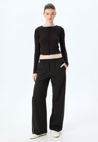 Zwarte cropped langermige shirt met ruwe randdetails, gecombineerd met losse zwarte broeken met een elastische tailleband en zijzakken.