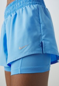 Pantalones cortos deportivos de color azul claro con cinturilla elástica, que presentan un logo de Nike bordado en plata y pantalones ajustados interiores para mayor soporte.