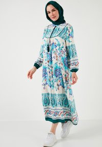 Long, loose-fitting dress in white with blue and pink floral patterns. Features a high neckline, long sleeves, and green accents.