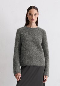 Donkergrijze, fluffy gebreide trui met een ronde hals en lange mouwen, gedragen over een zwarte rok, met een zachte textuur.