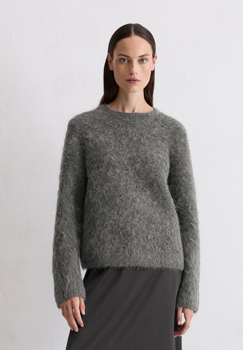 Pull en tricot gris foncé et moelleux avec un col rond et des manches longues, porté sur une jupe noire, présentant une texture douce.