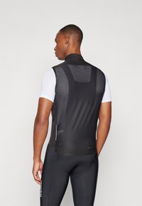 Zwarte fietsvest met mesh achterkant, hoge kraag en een getailleerd ontwerp. Draagt een wit T-shirt met korte mouwen en zwarte fiets-short.